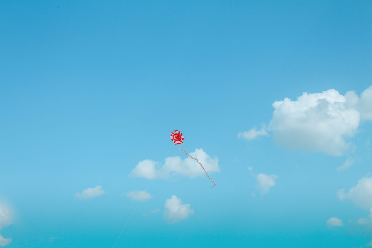 a vibrant red kite soaring in a clear blue sky with fluffy clouds