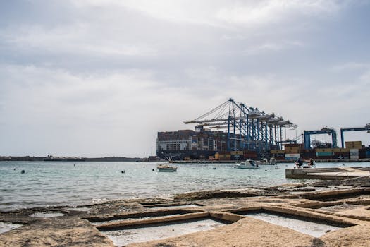 A vibrant harbor scene with cargo cranes and freight ships at a busy port against a cloudy sky.