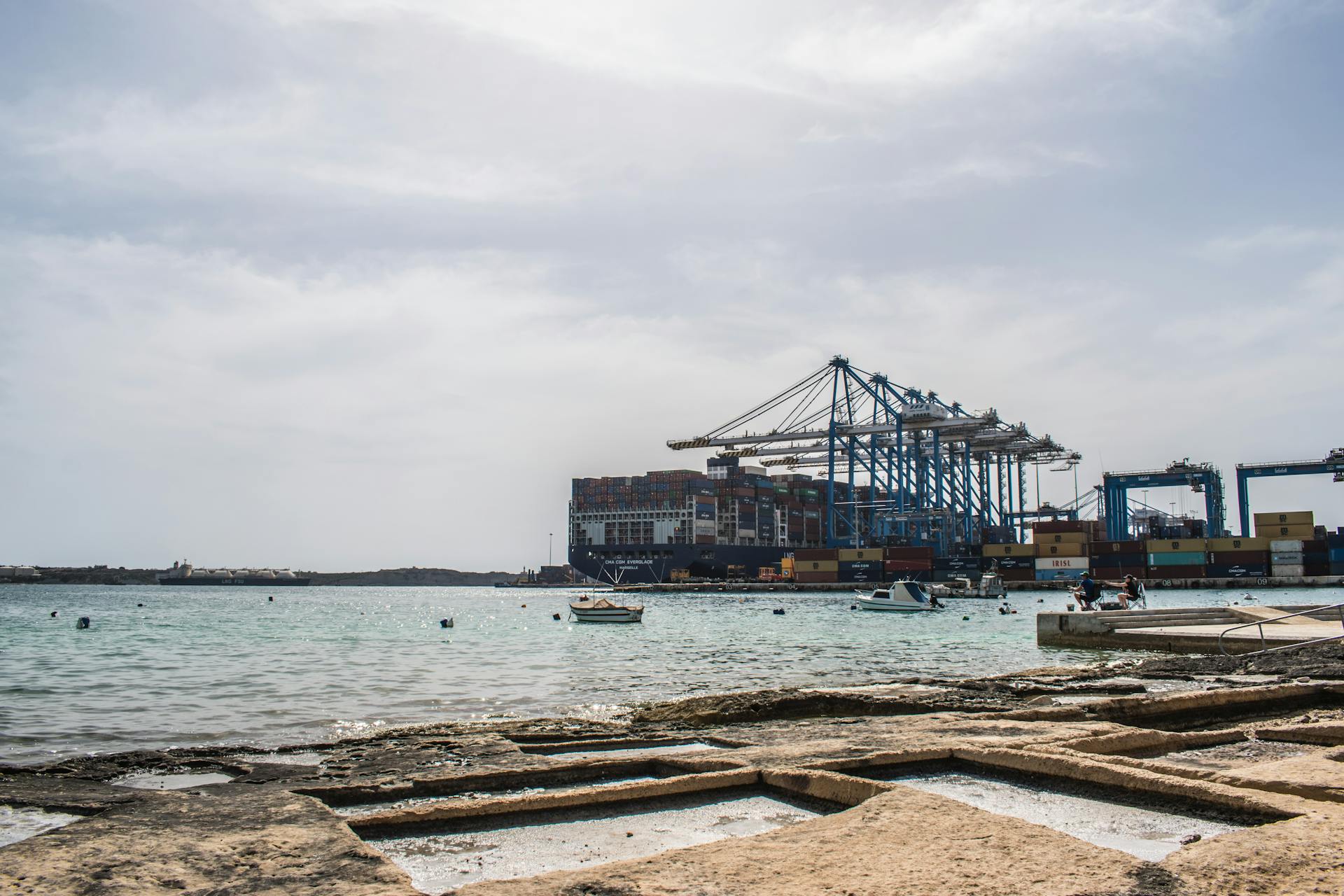 A vibrant harbor scene with cargo cranes and freight ships at a busy port against a cloudy sky.