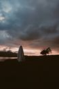 Person Wearing a Sheet under Dramatic Sky at Sunset