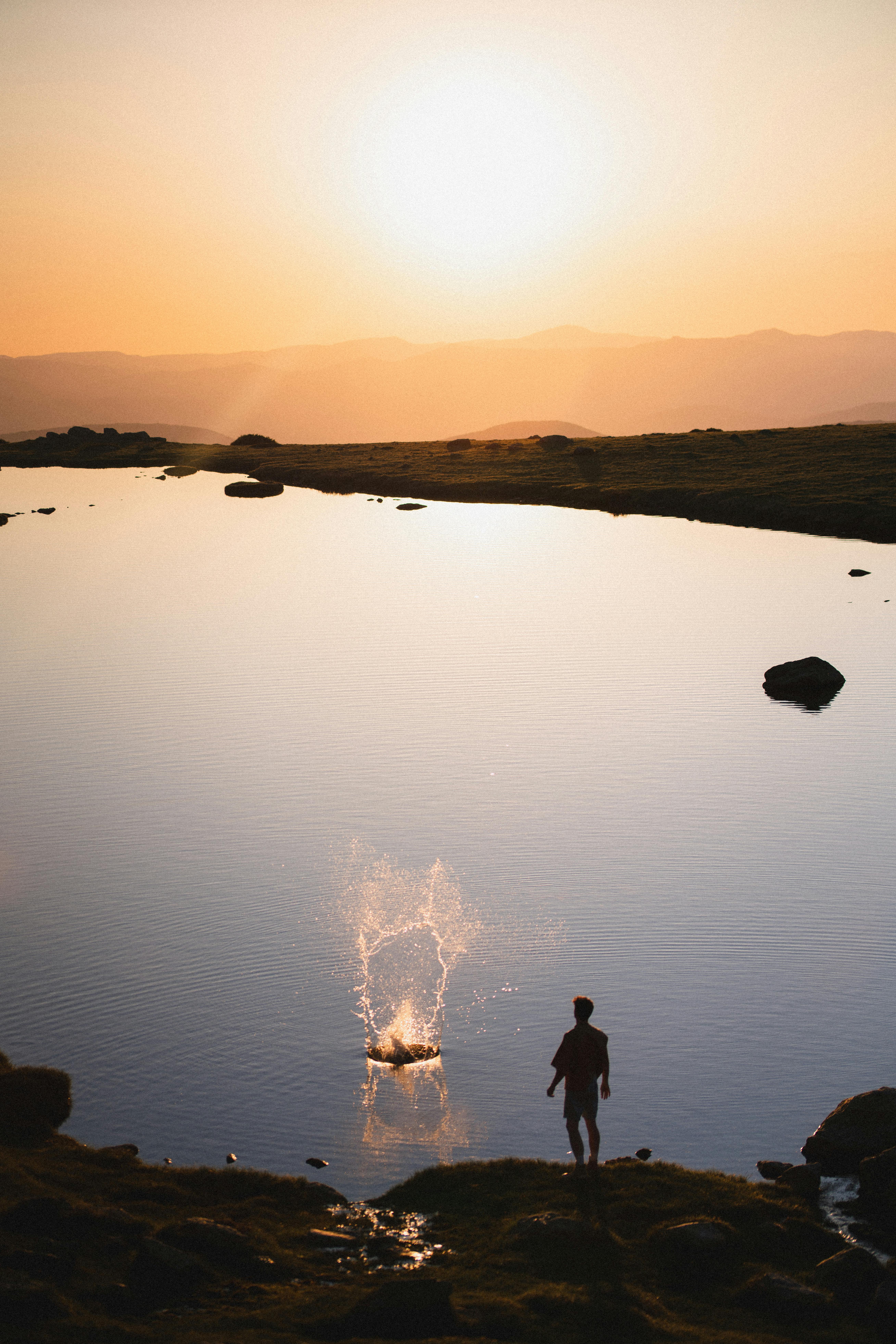 A man stands by a calm lake during sunset, creating a serene silhouette.