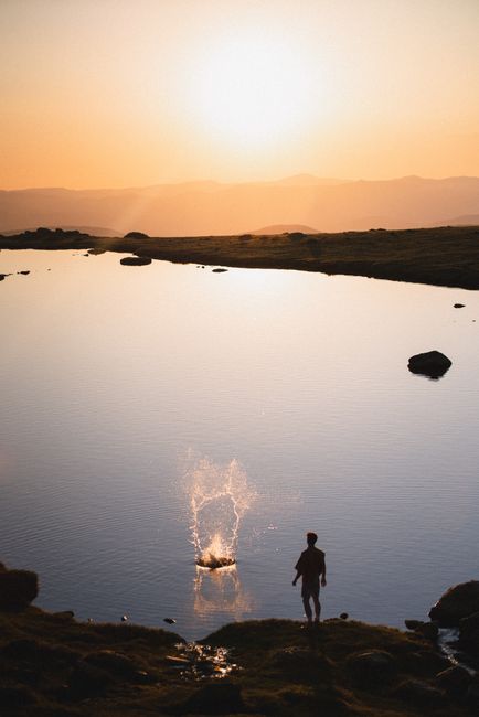A man stands by a calm lake during sunset, creating a serene silhouette.