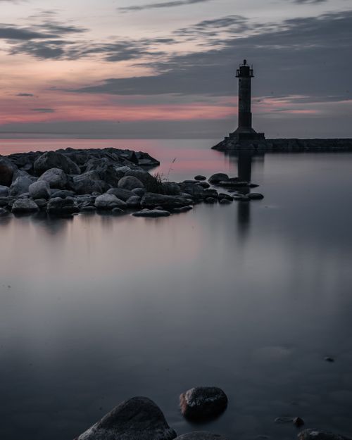 Free A tranquil sunset scene with a lighthouse standing guard over a rocky coastline and calm sea. Stock Photo