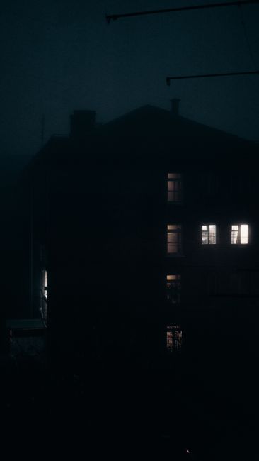 A dark urban building with lit windows, creating a mysterious night scene.