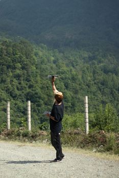 Man standing on a path surrounded by lush greenery, controlling a drone in daylight.