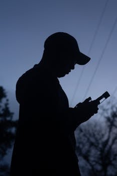 Silhouette of an adult holding a smartphone at dusk, capturing a serene and contemplative moment.