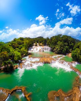 A breathtaking aerial view of Agua Azul Waterfalls, showcasing vibrant blue water and lush greenery under a clear sky.