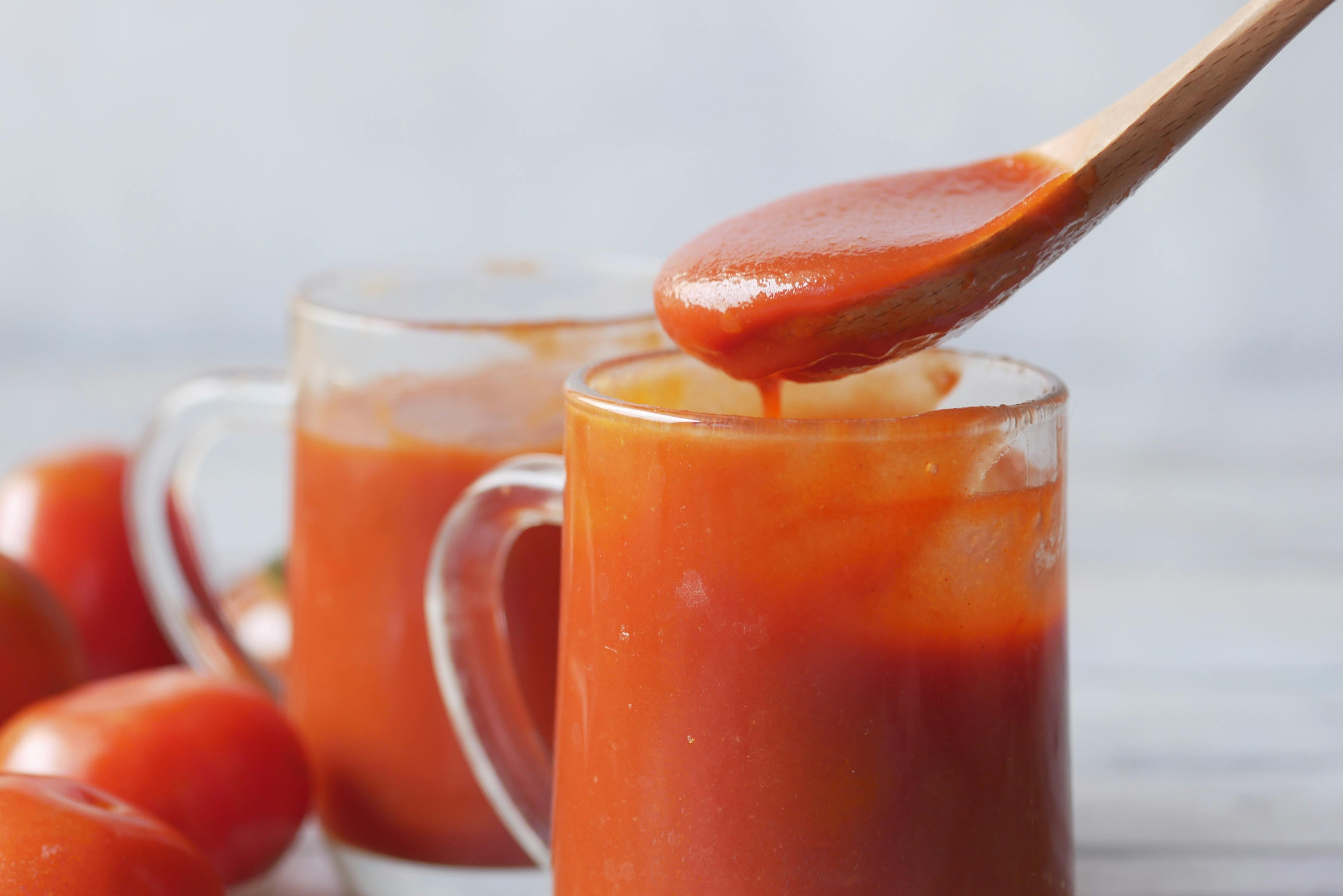 Close-up of tomato sauce in glasses with tomatoes beside them.