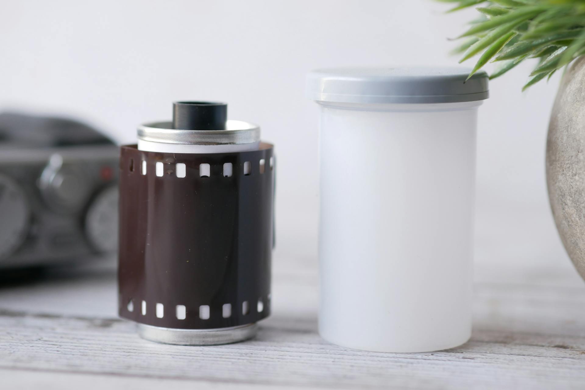 Close-up of a vintage camera film roll and plastic container on a wooden table. Ideal for photography nostalgia.