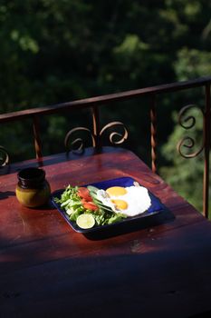 A vibrant breakfast with eggs, salad, and lime on a balcony in the morning sunlight.