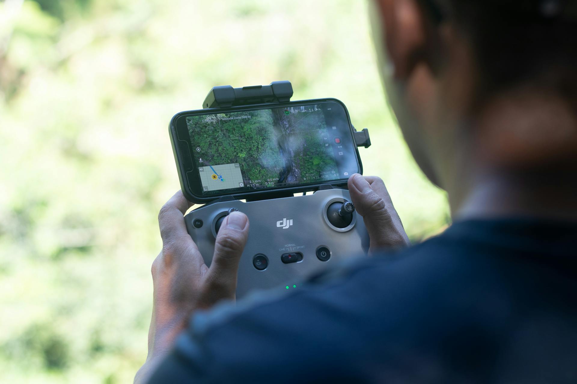 Close-up of a drone controller held by a person with a smartphone displaying aerial footage.