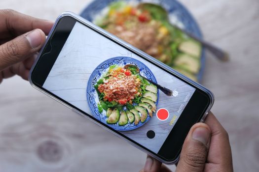 Close-up of hands taking a mobile photo of a vibrant salad dish.
