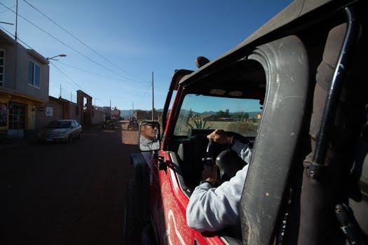 Person driving an off-road vehicle through a rural town under a clear blue sky.