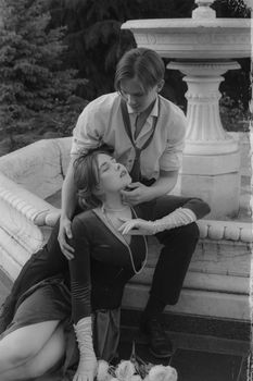 Black and white photo of a romantic couple by a classic fountain, exuding intimacy and love.
