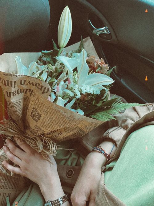 Free Elegant bouquet of lilies and flowers wrapped in paper, gently held in a car seat, creating a warm and vibrant mood. Stock Photo