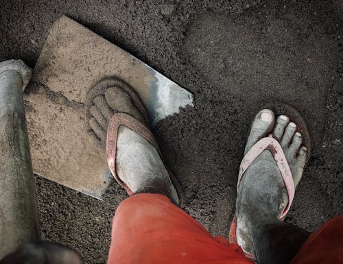 A Person in Red Shorts Wearing Slippers on Brown Soil