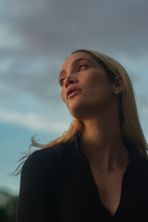 Free Low-angle portrait of a woman with blond hair looking away, captured outdoors at dusk. Stock Photo