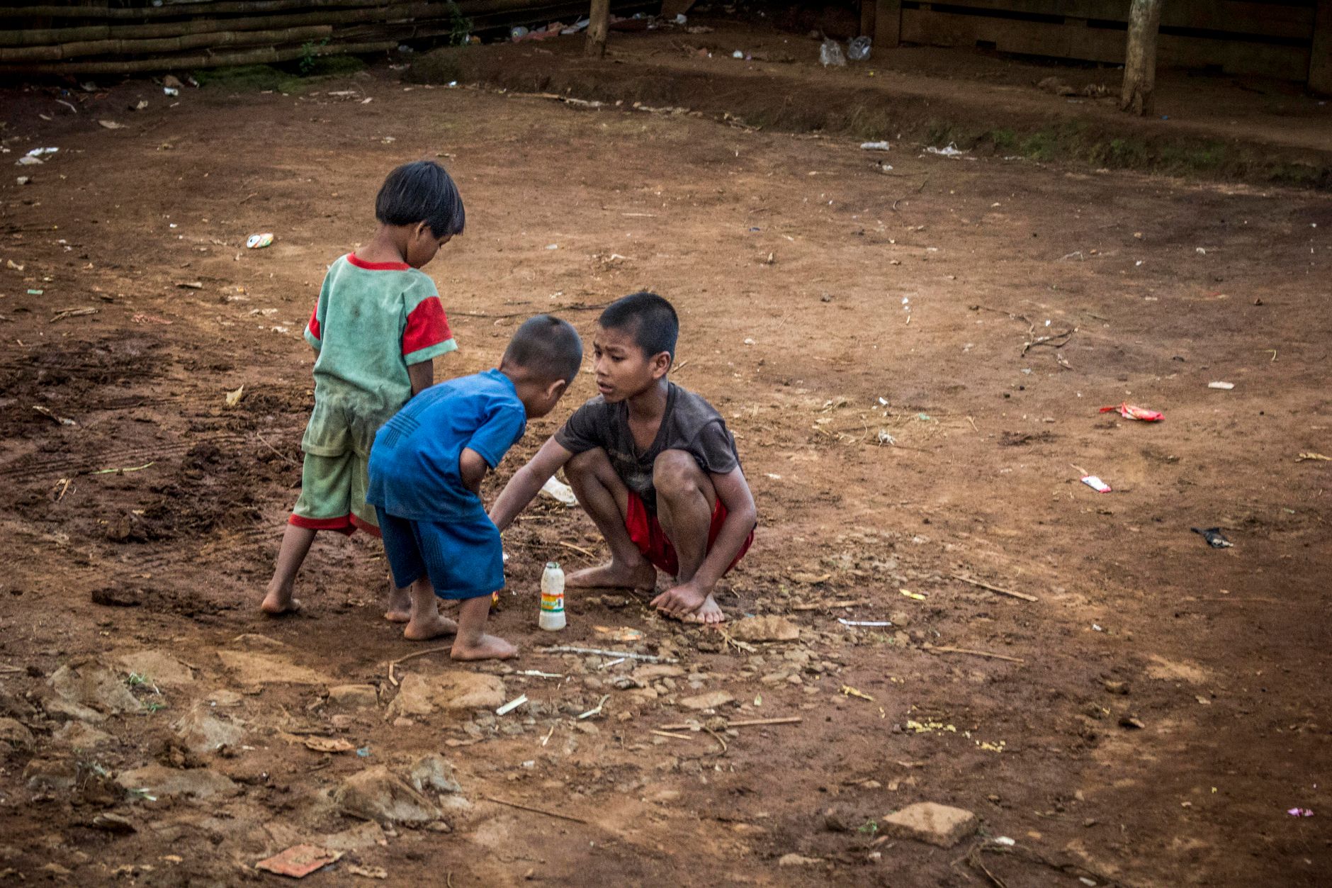 Three young children playing on a dirt path, depicting playful interaction in a rural setting.