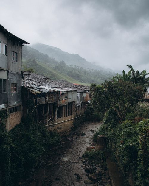 Free Charming village tucked in lush mountains with overcast skies and rustic houses by a stream. Stock Photo