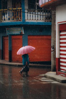 A person with an umbrella walking through a colorful urban street during a rainy day.