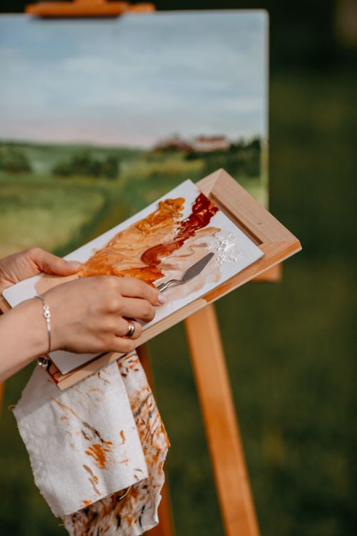 Free Artist holds palette while painting landscape outdoors, blending vibrant colors. Stock Photo