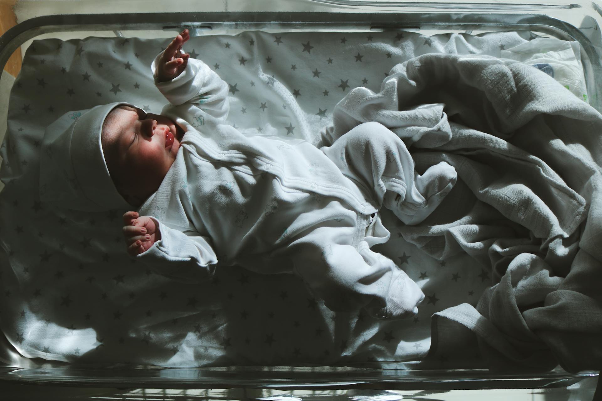 Newborn baby peacefully sleeping in a hospital cot with soft lighting and warm tones.