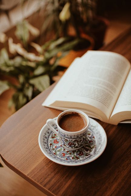 A beautifully designed coffee cup sits next to an open book on a wooden table, creating a warm, inviting atmosphere.