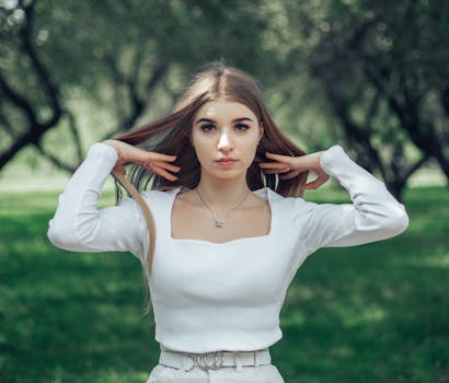 Young woman in white top standing in a green park setting.