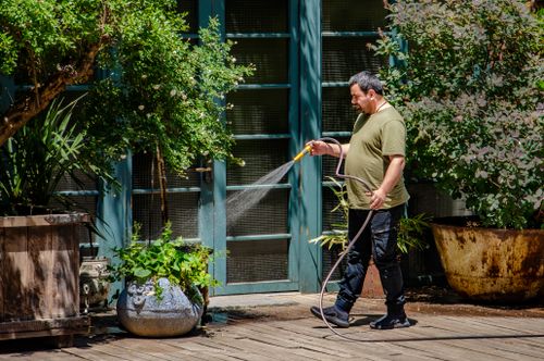 Free A man attentively waters plants on a sunny garden patio, emphasizing outdoor care and greenery. Stock Photo