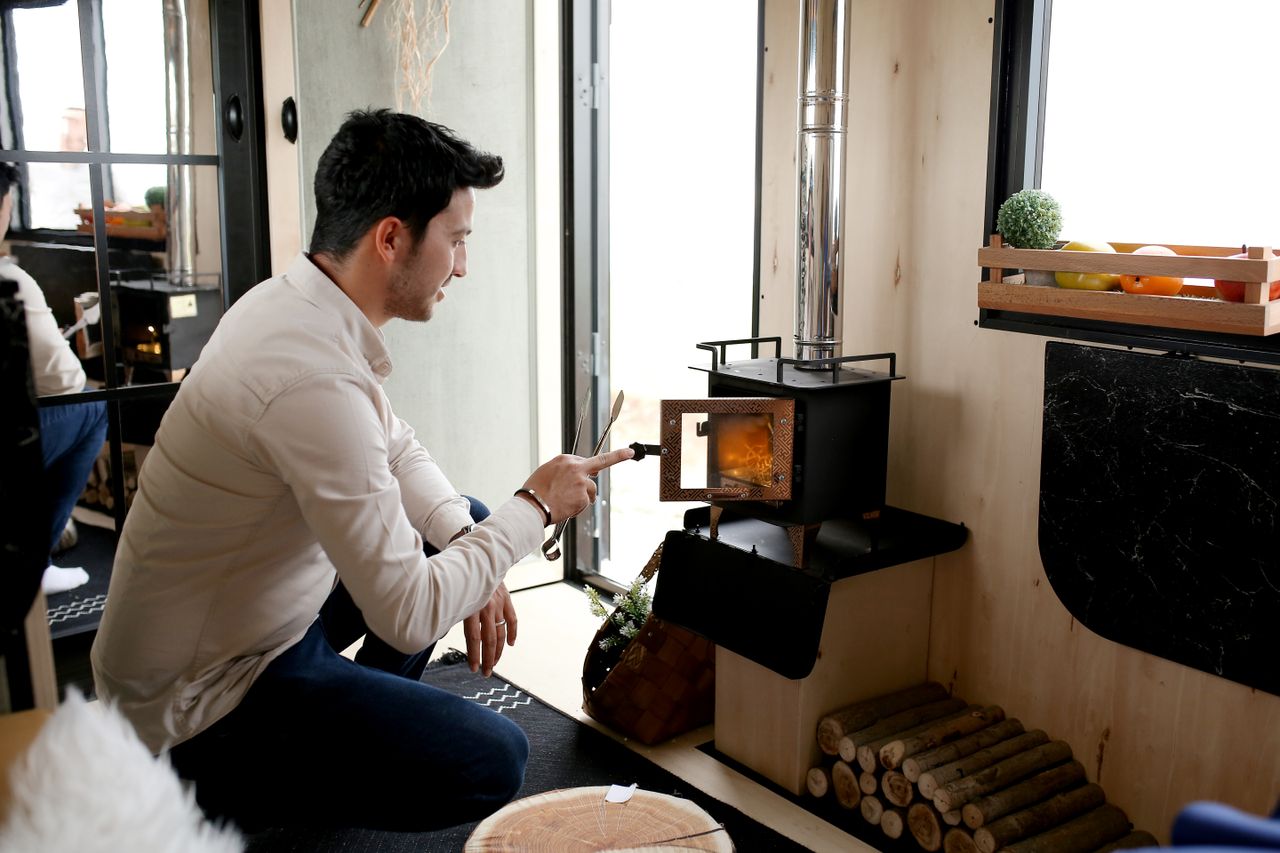 Small black log burner with a neat stack of firewood stored underneath it in a compact cottage room