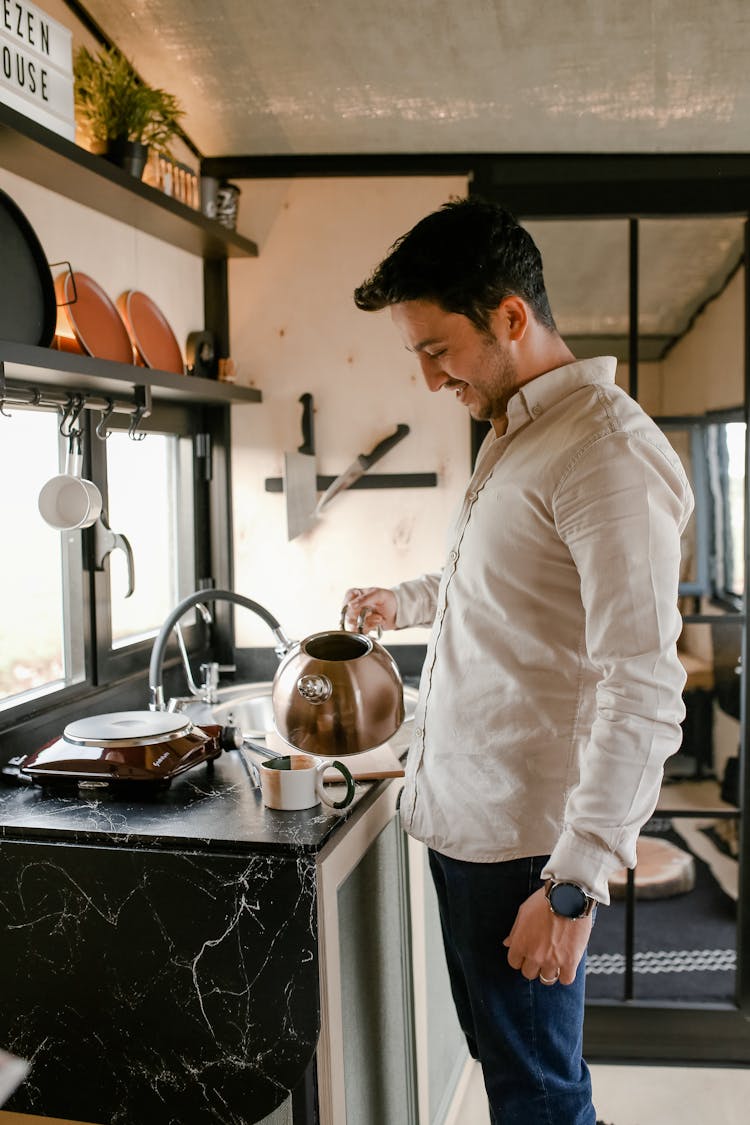 Man Pouring Water From Kettle To Cup In Kitchen