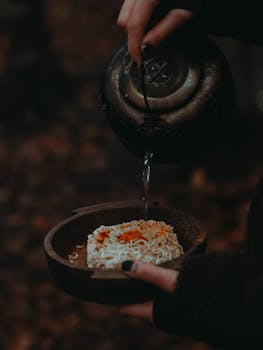 An artistic close-up of hot water being poured over instant noodles in a rustic setting.