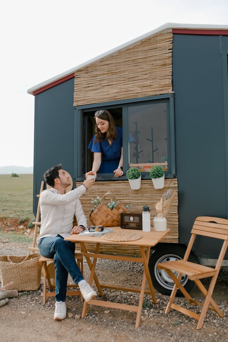 Woman Serving Cup Of Tea From Kitchen Window To Her Partner