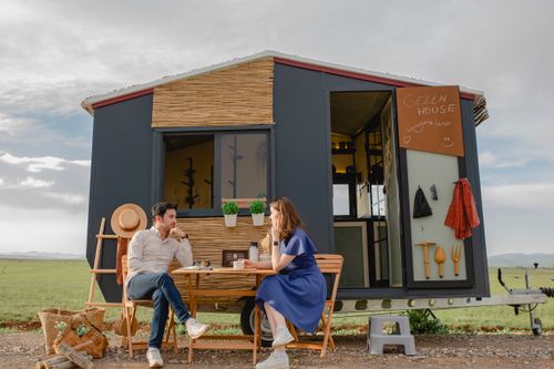 Free A young couple relaxing at a picnic table outside a modern tiny home in nature. Stock Photo