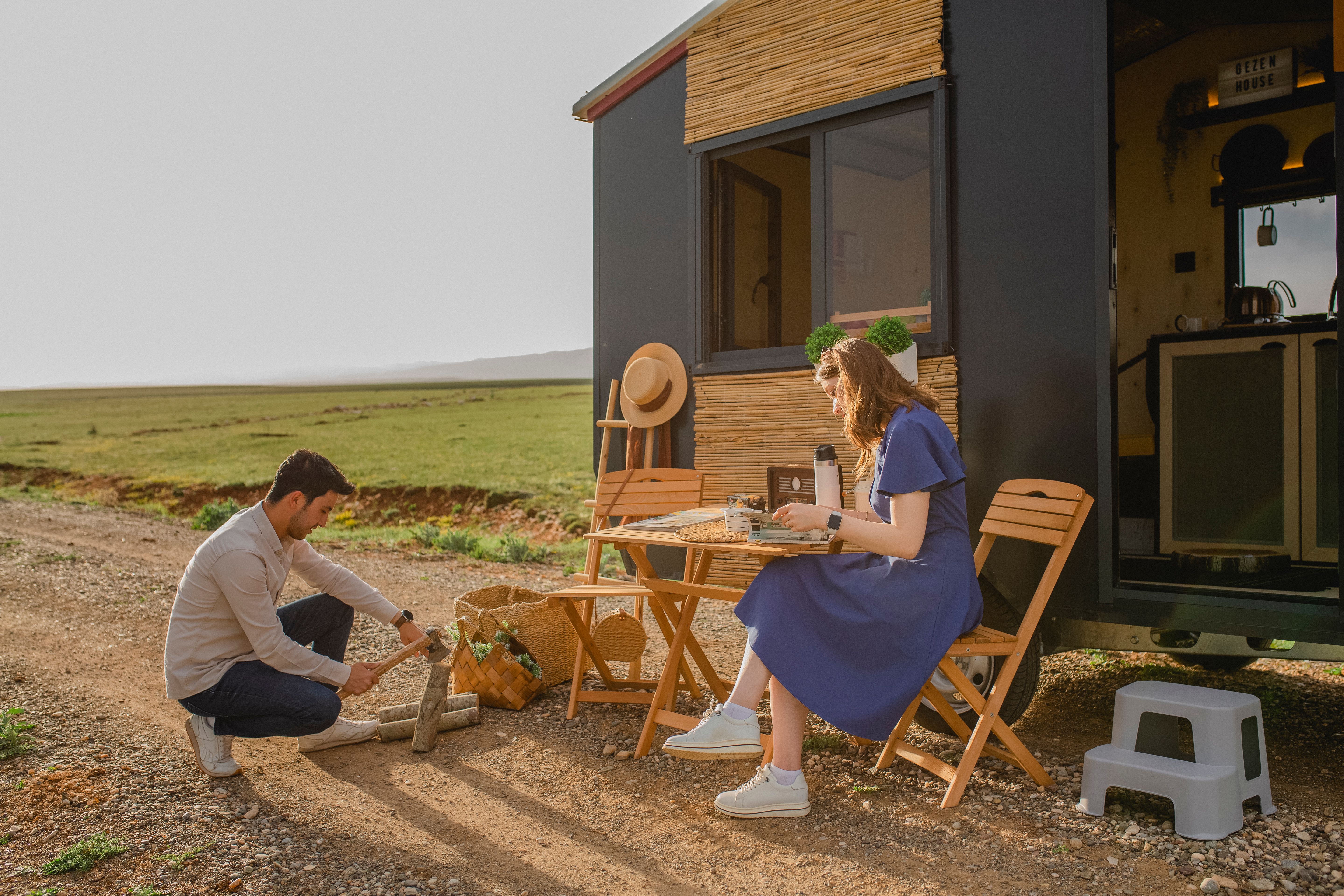 A couple enjoys a meal outdoors by their camper on a sunny day, embracing a travel lifestyle.