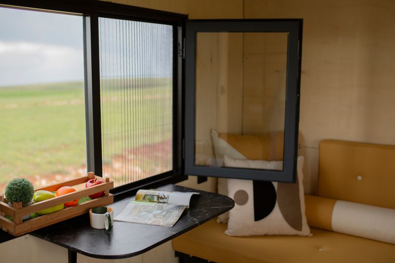 A charming tiny house interior with a window view of nature, featuring a compact dining area.