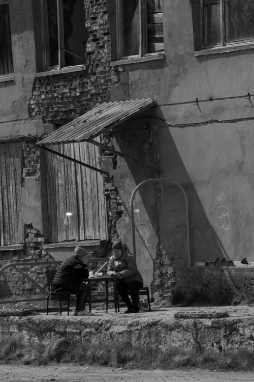 Free Black and white photo of two people playing chess outside a dilapidated urban building. Stock Photo