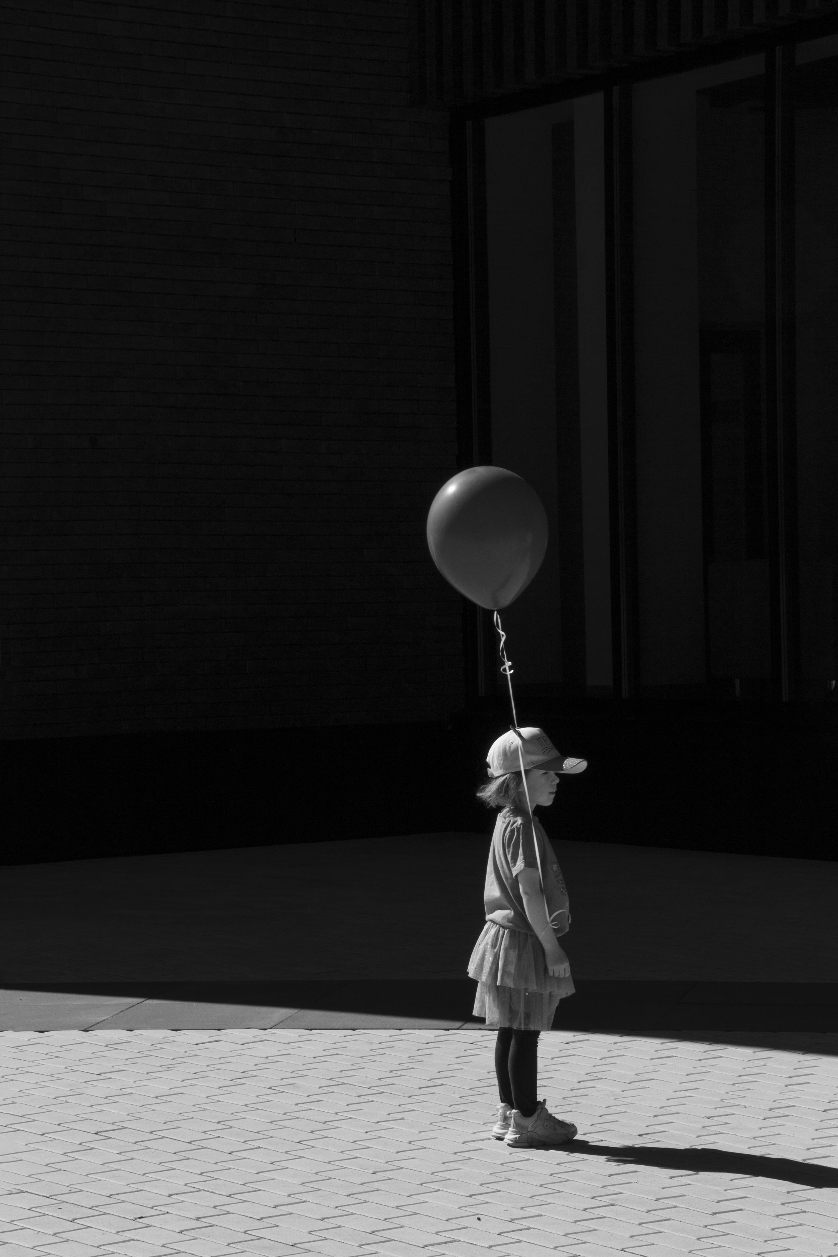 A child in a hat holding a balloon in a stark black and white indoor setting.