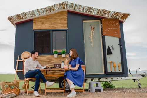 Free Couple sitting and talking outside a stylish camper house in a scenic outdoor setting. Stock Photo