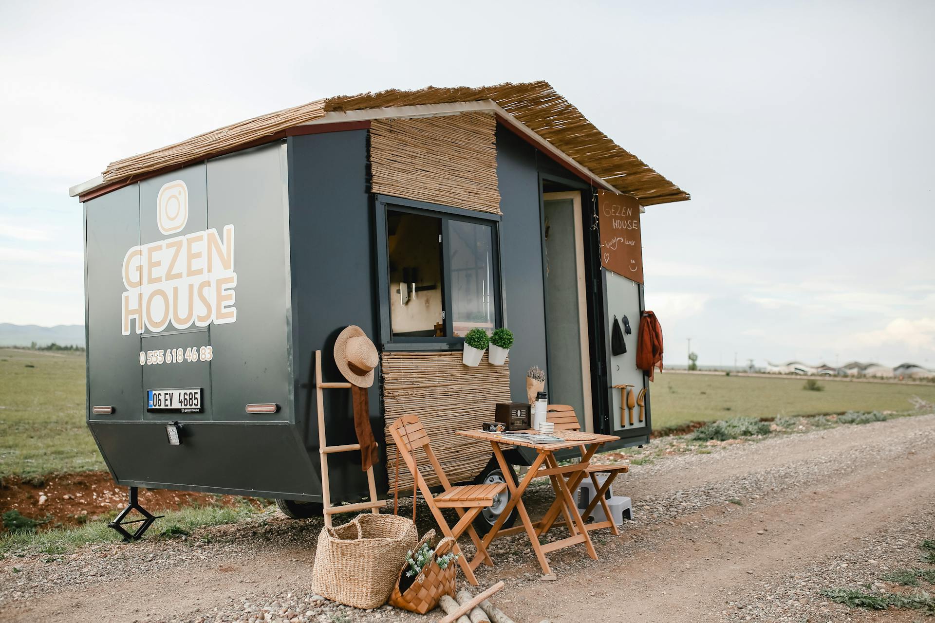 Mobile tiny house with outdoor furniture on a countryside dirt road.