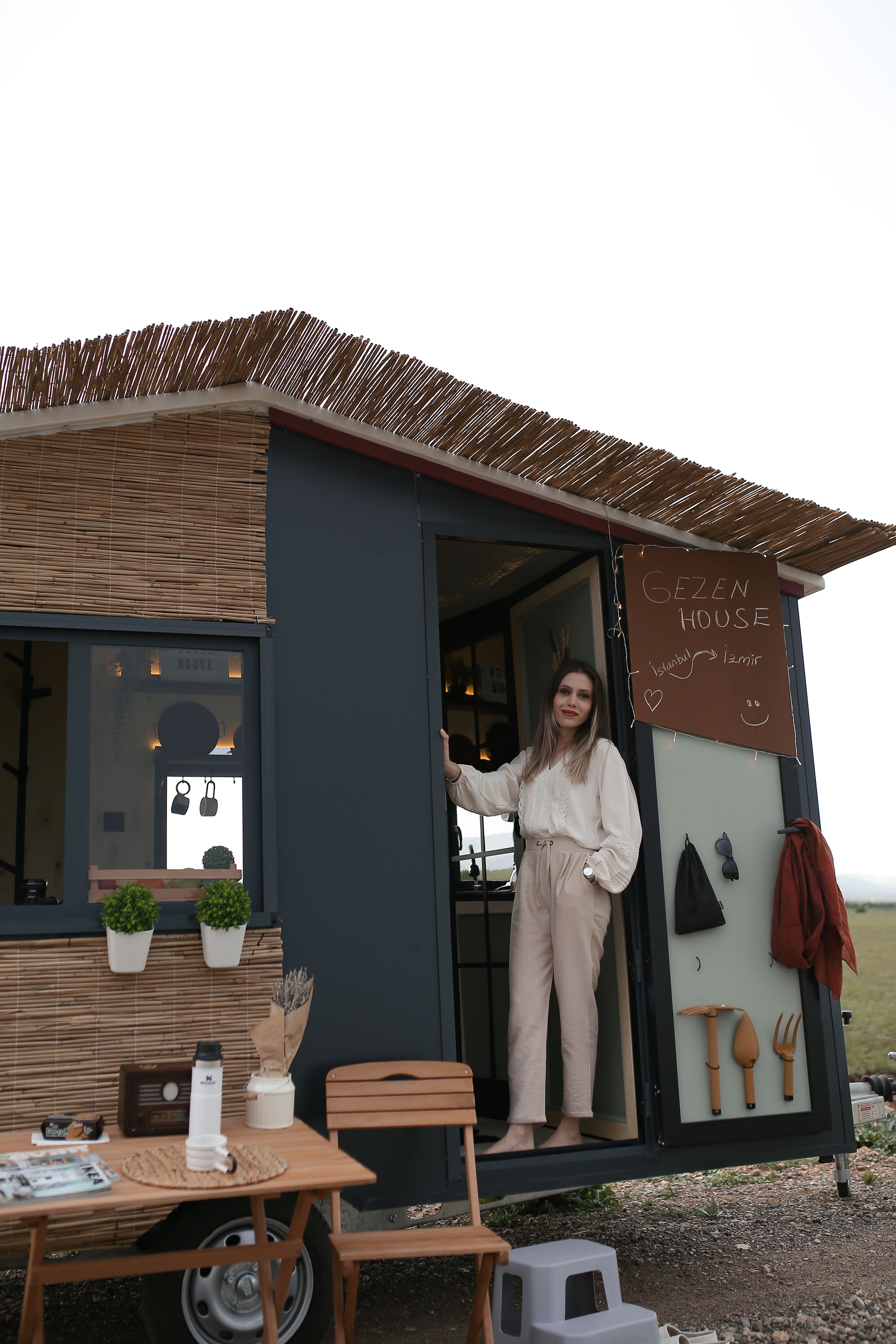 Young woman stands at the door of a stylish mobile home with rustic elements and outdoor decor.