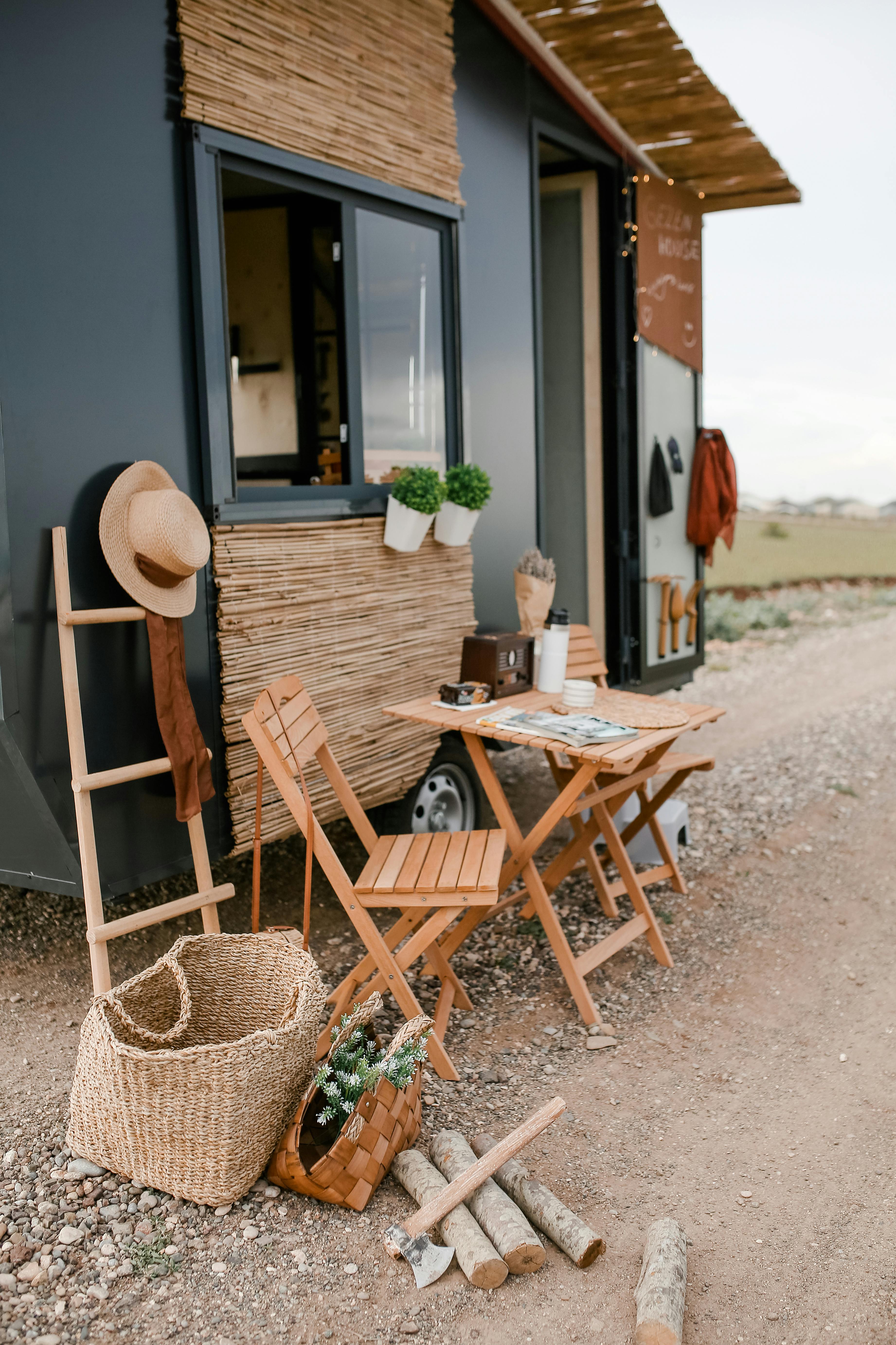Free Rustic outdoor dining setup beside a modern tiny home with wicker baskets and wood elements. Stock Photo