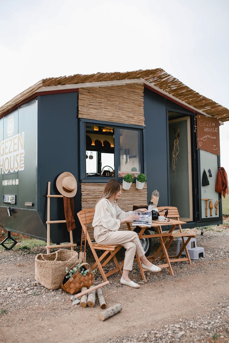 Woman Sitting In Front Of A Trailer Converted To A House On Wheels