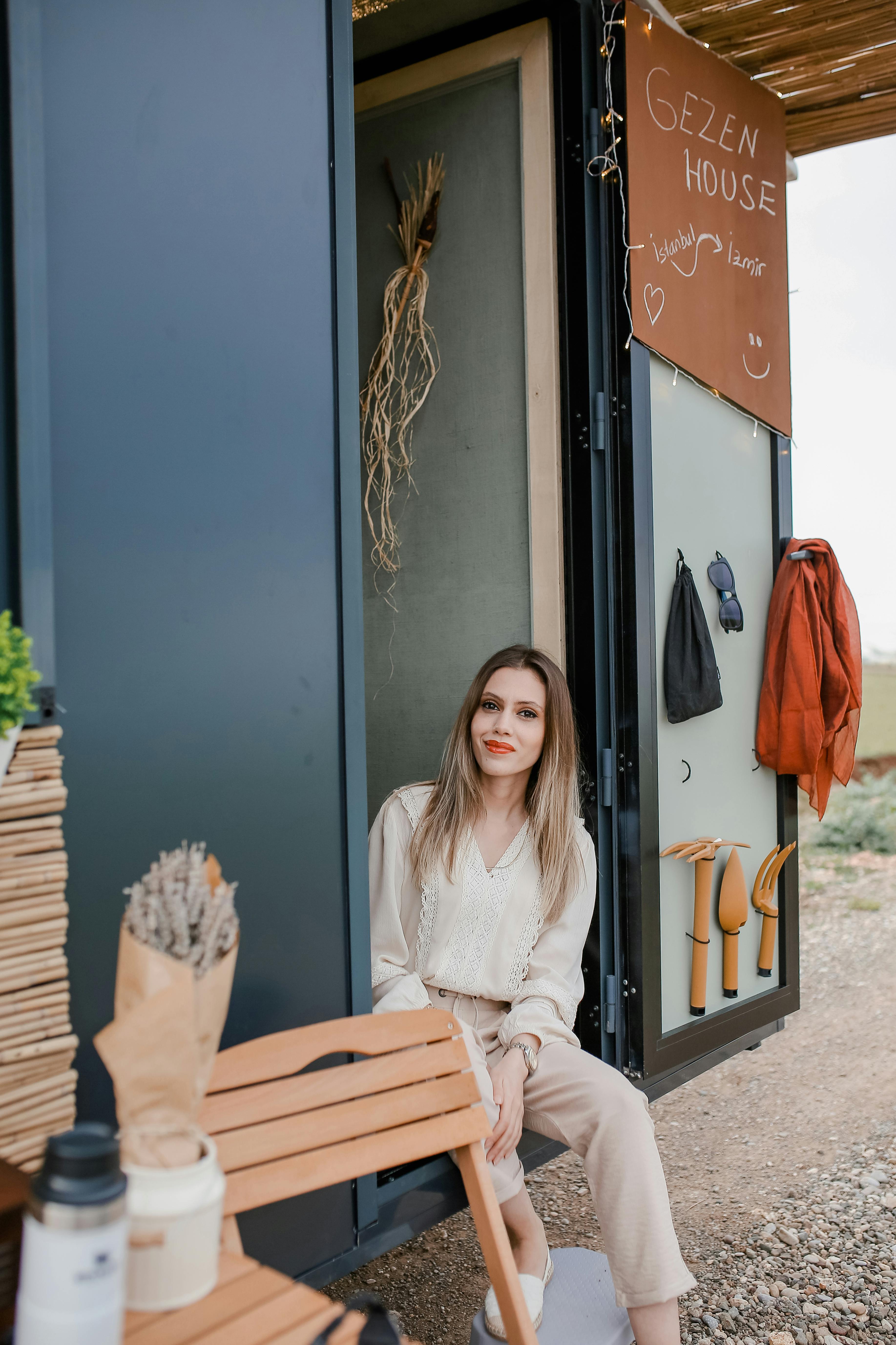 Free Woman sitting and smiling at the entrance of a tiny mobile home, enjoying the outdoor ambiance. Stock Photo