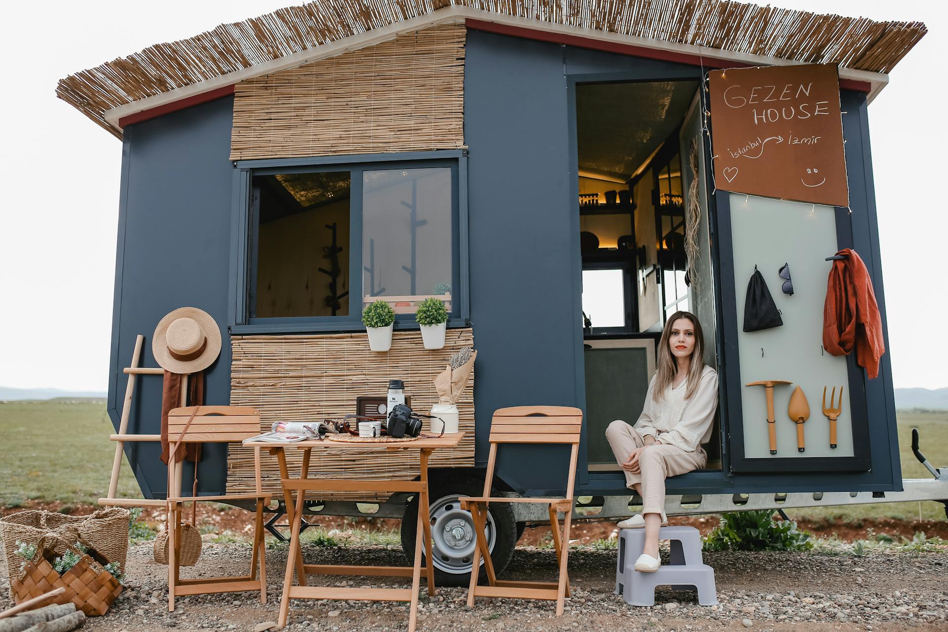 A woman relaxing outside her modern tiny mobile home in a scenic outdoor setting.