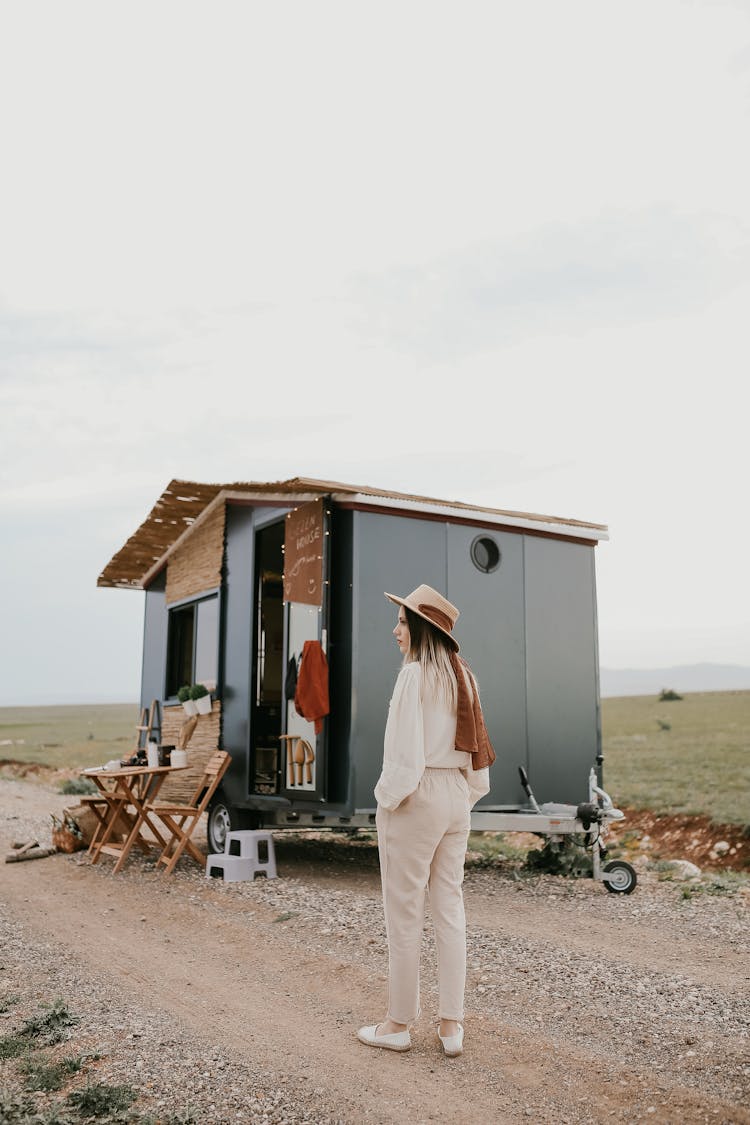 Woman Standing In Front Of A Trailer Converted To A House On Wheels