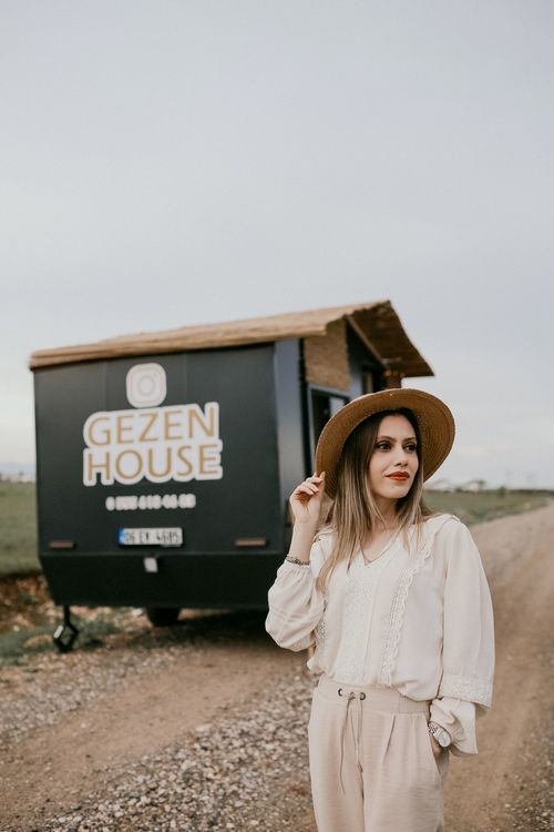 Free Fashionable woman wearing a brown hat posing beside a mobile home on a rural road. Stock Photo