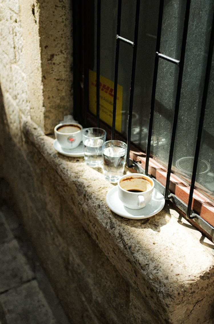 Dirty Cups With Coffee Leftovers And Glasses With Water Standing On A Windowsill Outdoors 