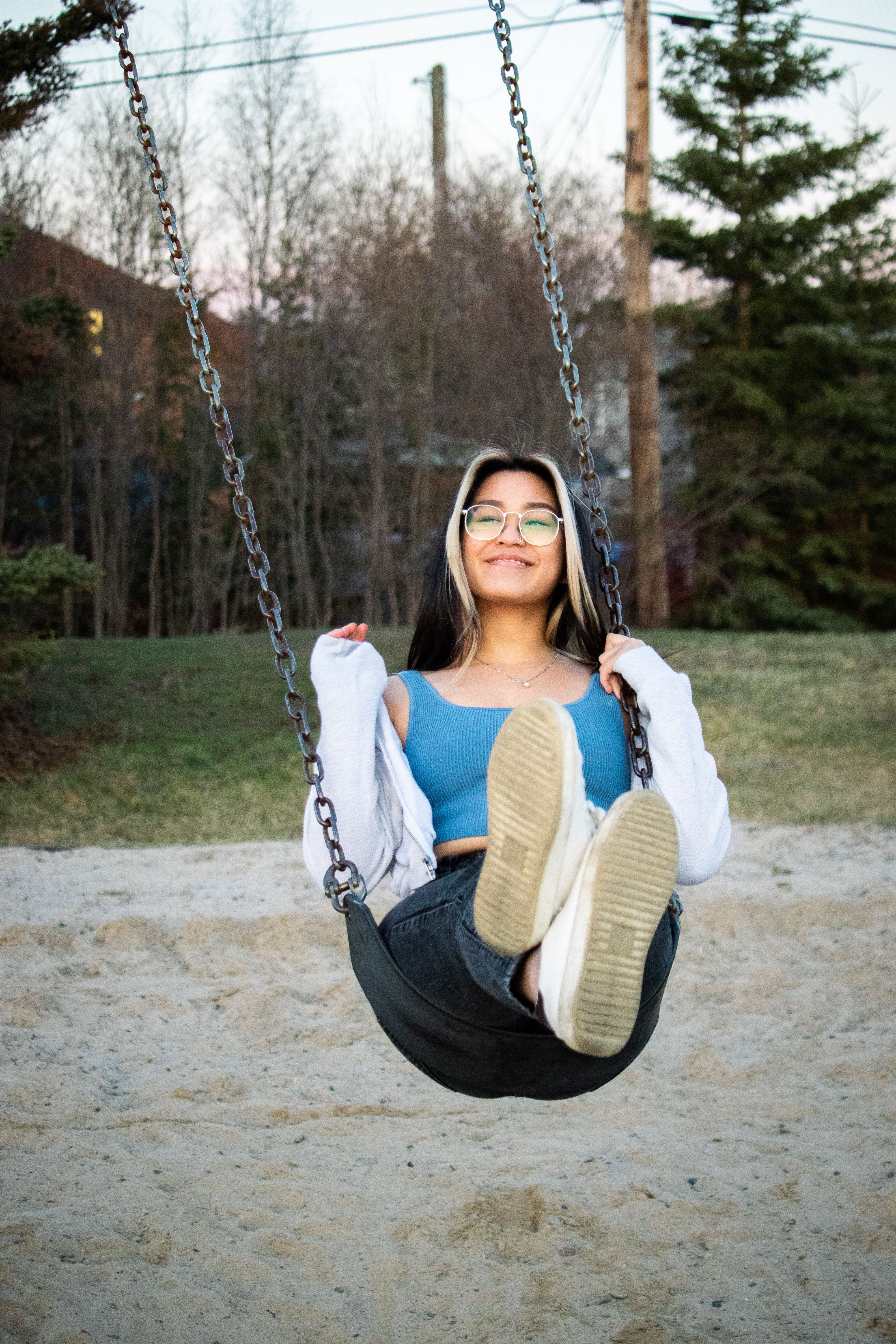 Smiling woman with eyeglasses swinging in a park during autumn. Captured in a joyful moment.