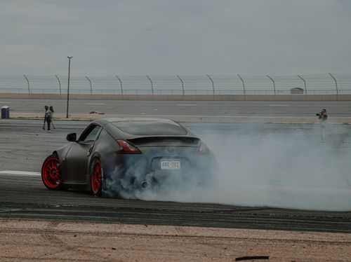 Free A Nissan sports car drifting on a raceway, surrounded by smoke and captured by photographers. Stock Photo